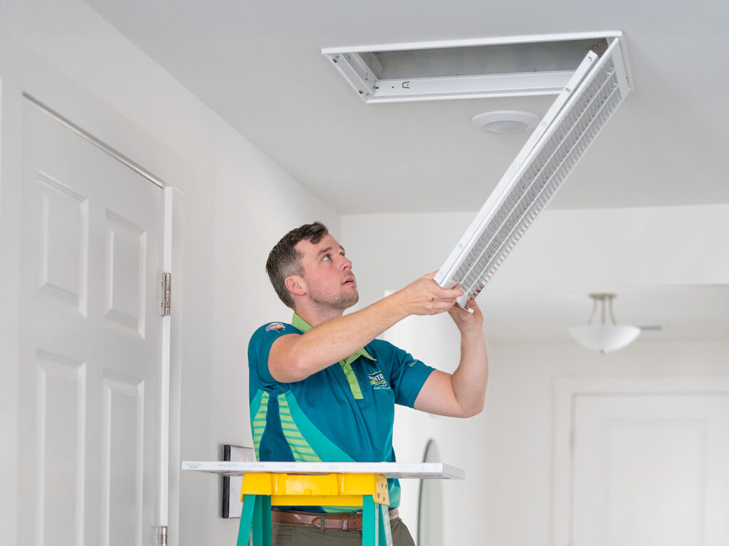 HVAC technician removing large ceiling air filter grille from vent