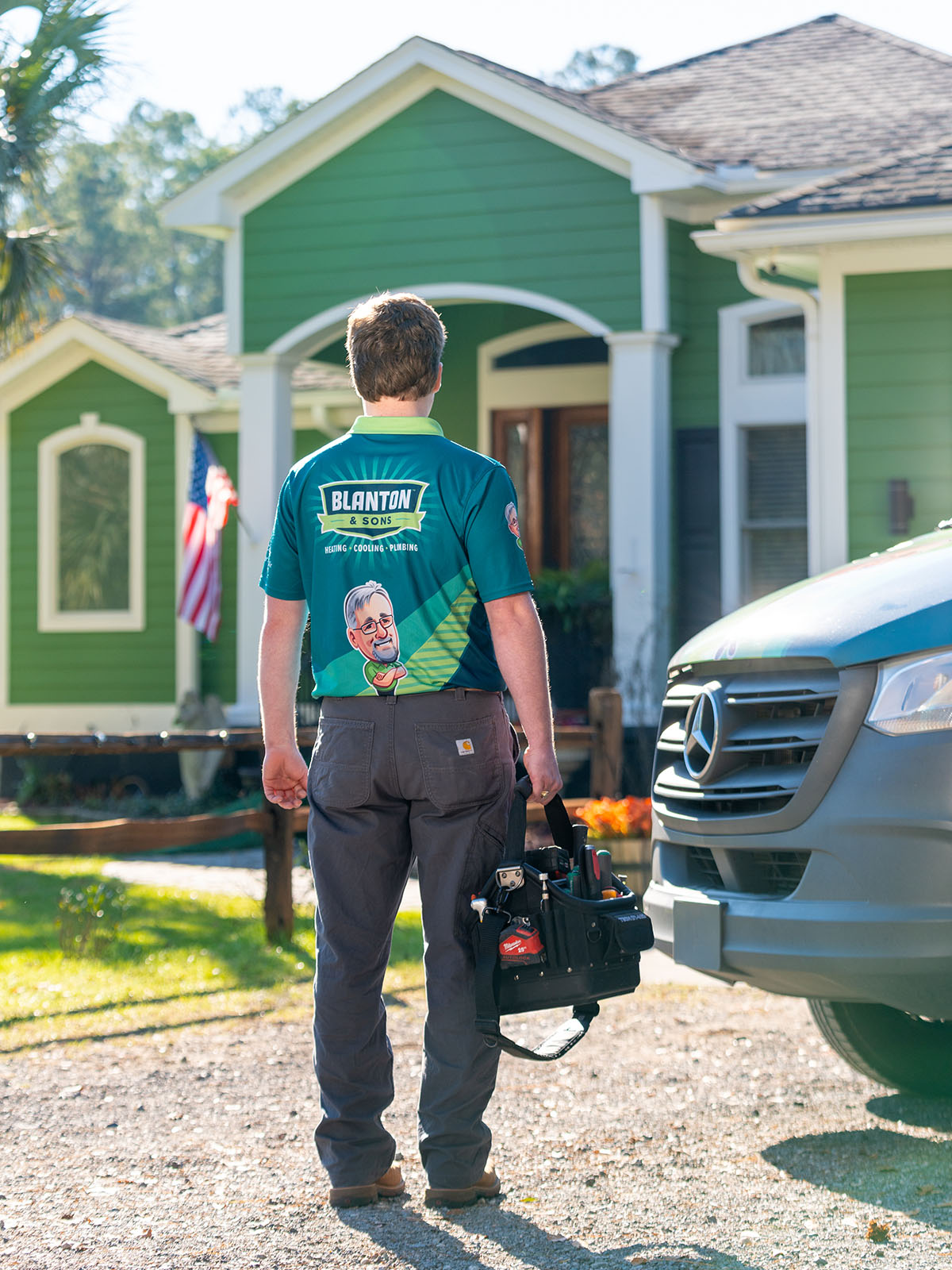 Blanton's technician stands in front of a house, holding a tool bag, ready for home repairs