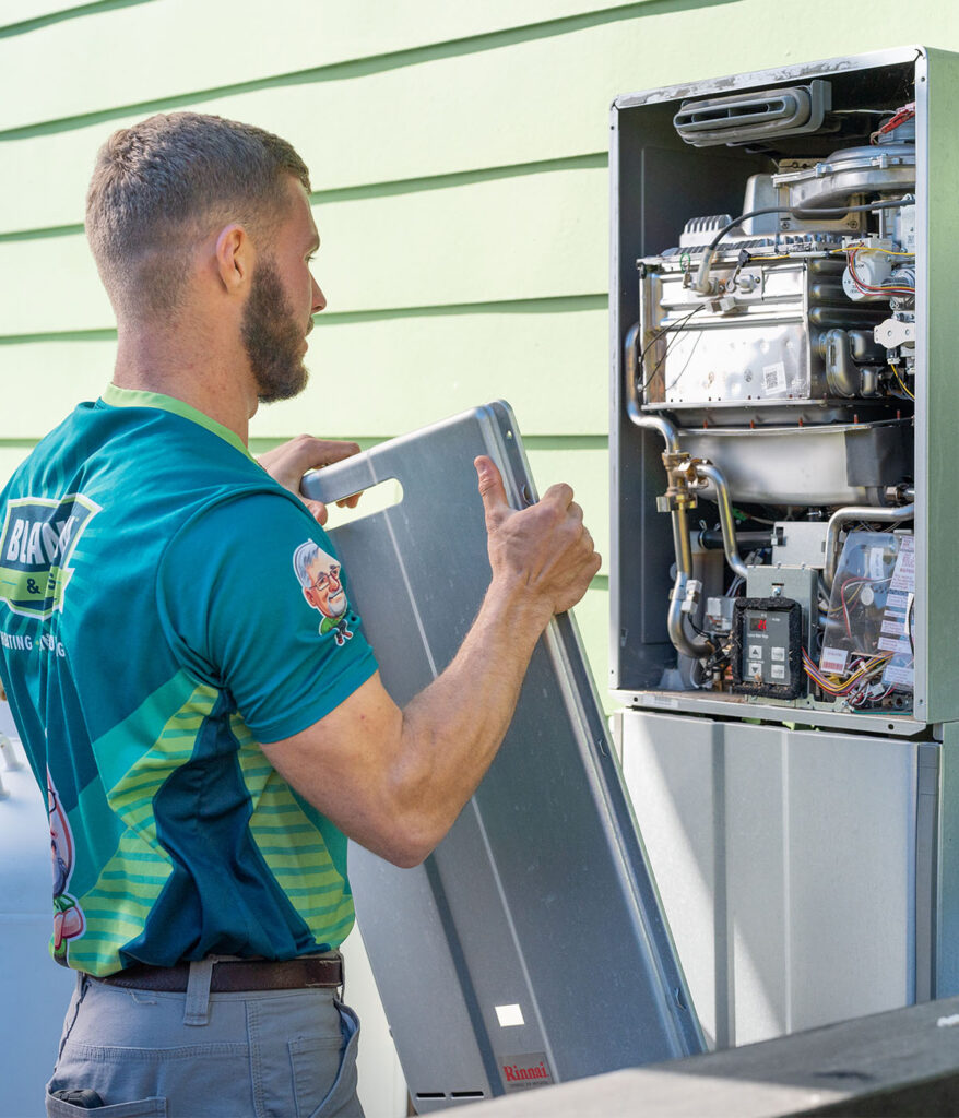 Technician removing access panel to inspect Rinnai tankless water heater unit
